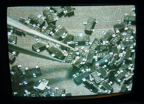 Using a video monitor to read the markings on a batch of SMD transistors and selecting one with tweezers.