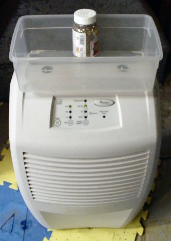 Dehumidifier with plastic container mounted on top and foam tiles underneath.