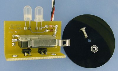PCB with a snap-action switch with a hole in it, a black plastic disc, a screw, and a nut.