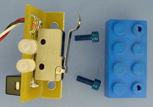 The circuit board mounts to a Lego block with tapped holes using blue anodized socket-head cap screws.