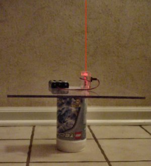 A laser pointer on a flat plate aims at a tall ceiling to measure parallelism.