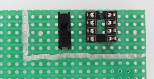 Perforated prototyping board with a DIP socket and a miniature switch.